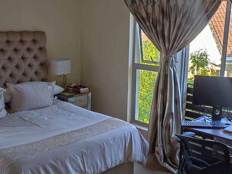 A well-lit bedroom featuring neutral walls, carpeted flooring, and large aluminium-framed windows that provide natural light and access to an outdoor balcony area.