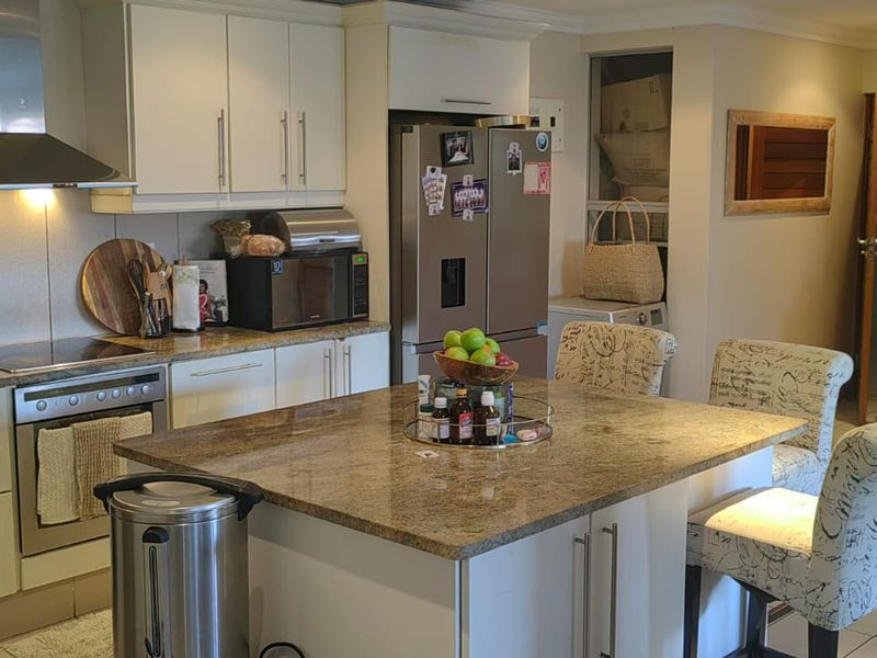 Open-plan kitchen featuring a central island with granite countertops, built-in cabinetry, and integrated appliances, seamlessly flowing into the adjacent living area.