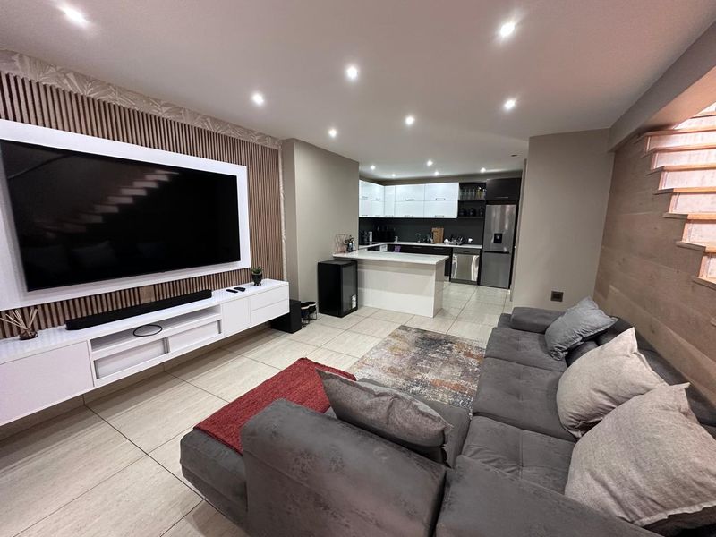 Modern open-plan living area featuring a sleek kitchen with island, tiled floors, and a contemporary timber slat feature wall with integrated media unit.