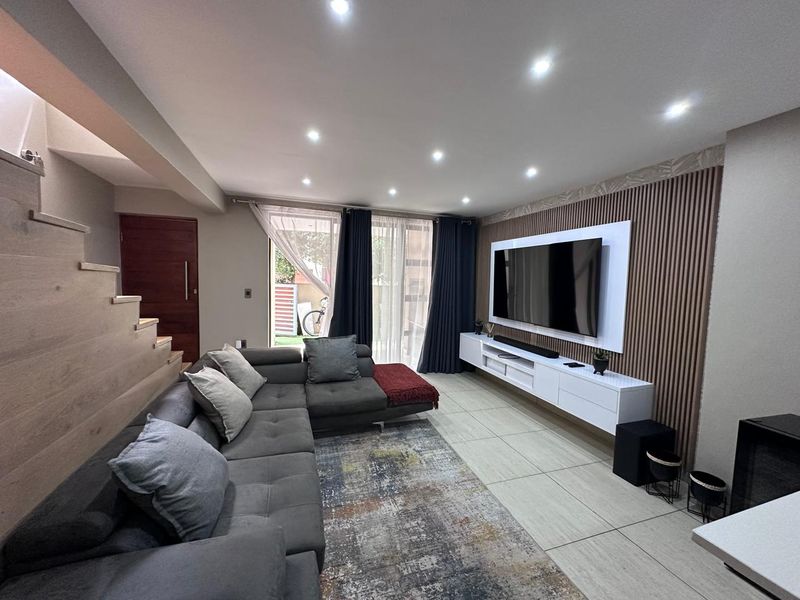 Modern living room featuring a feature slatted timber wall, built-in media console, recessed downlighting, and tiled flooring with an adjacent staircase.