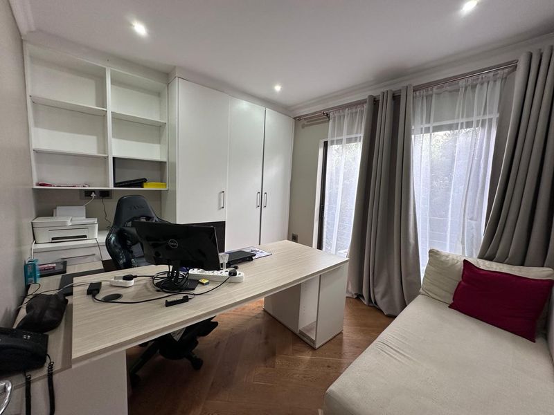 A functional home office featuring built-in shelving, ample storage cabinetry, herringbone timber flooring, and direct access to an outdoor area via sliding glass doors.