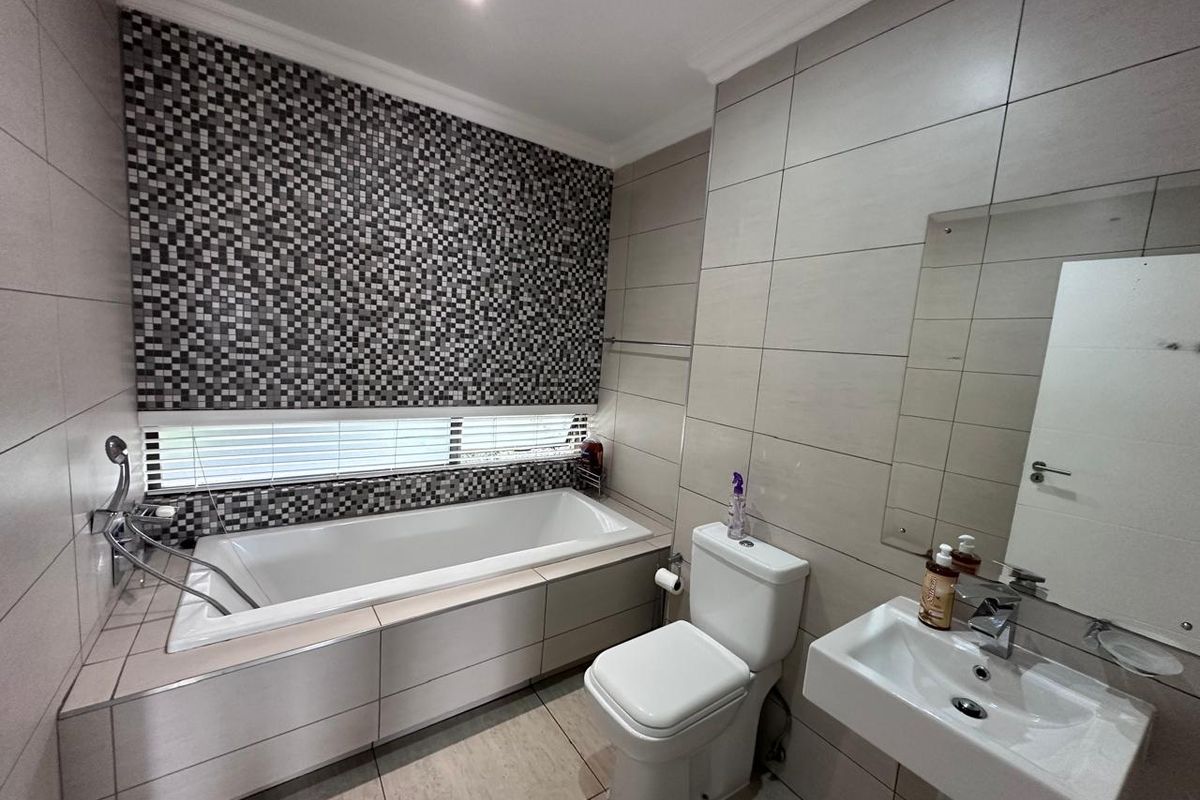 Modern bathroom featuring a built-in bathtub, mosaic tile accent wall, wall-mounted basin, and neutral floor-to-ceiling tiling.