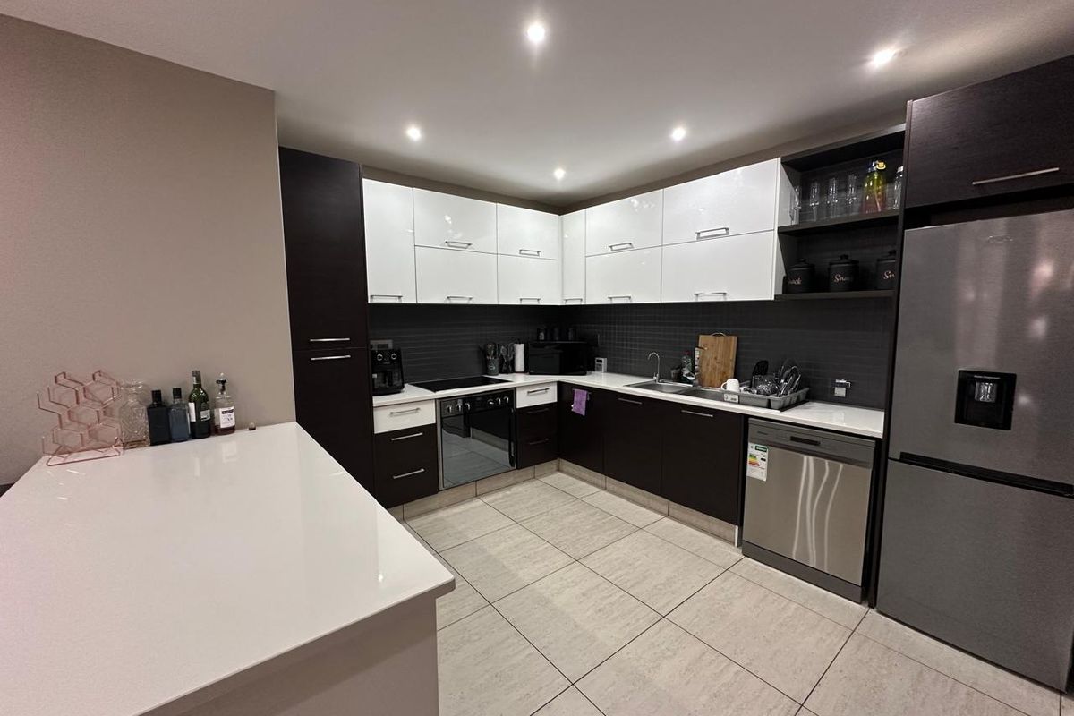 Modern kitchen featuring high-gloss cabinetry, stone countertops, integrated appliances, and tiled flooring with recessed lighting.