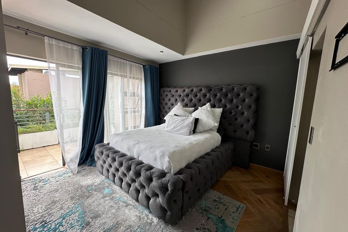 A well-maintained bedroom featuring herringbone timber flooring, recessed lighting, and direct access to a private balcony through sliding glass doors.