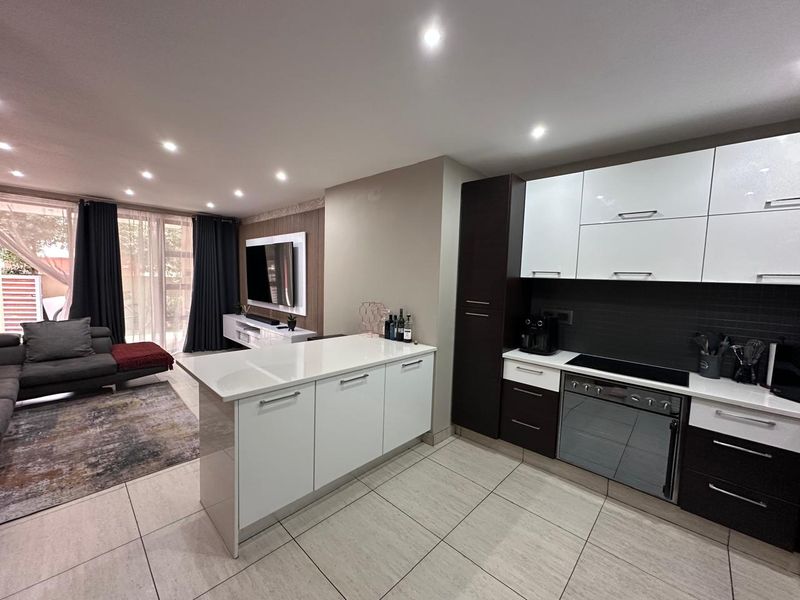 Modern open-plan living area featuring a sleek kitchen with white and dark cabinetry, quartz countertops, integrated appliances, and seamless flow to the lounge.