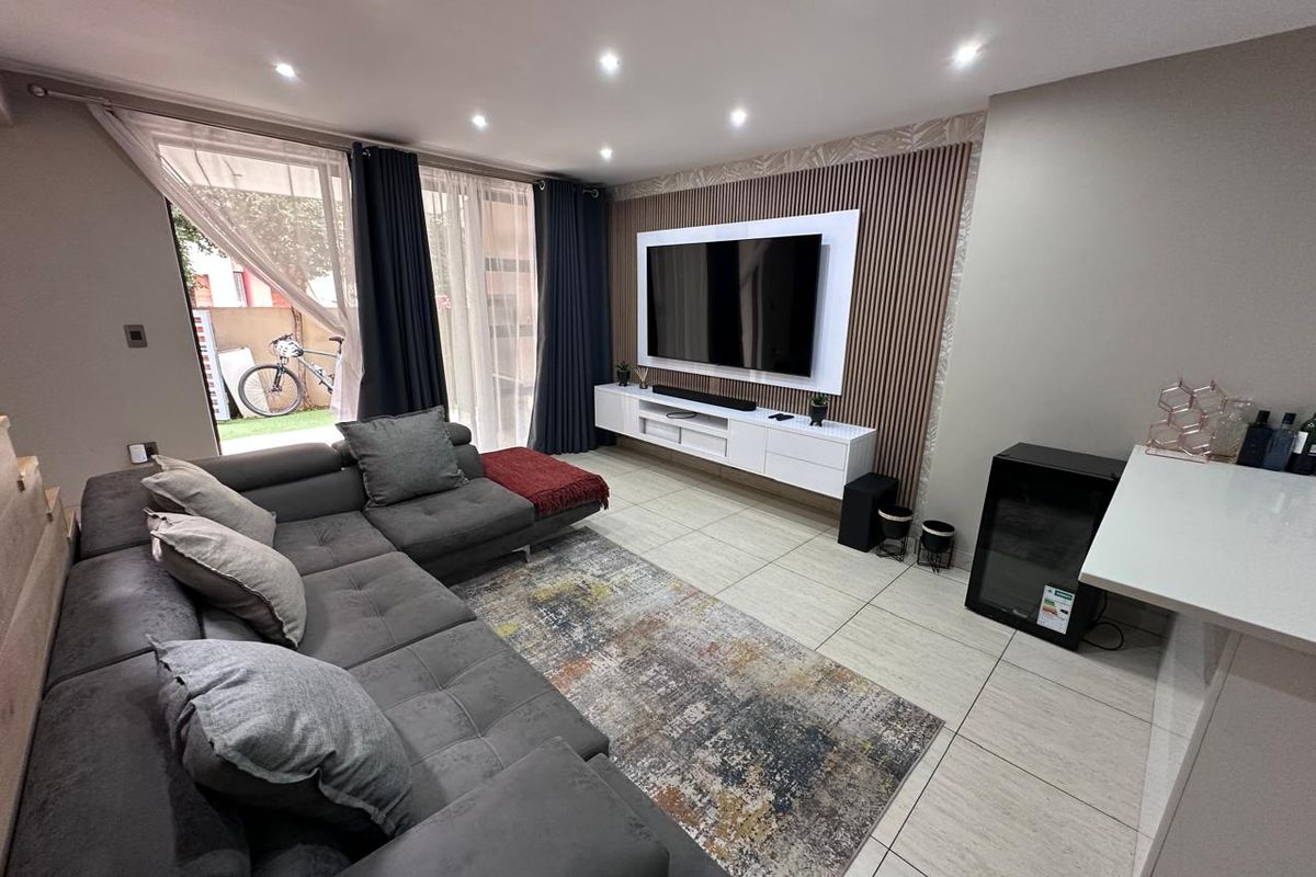 Modern living room featuring tiled floors, recessed lighting, and a stylish slatted timber feature wall with a built-in media console and sliding door access.