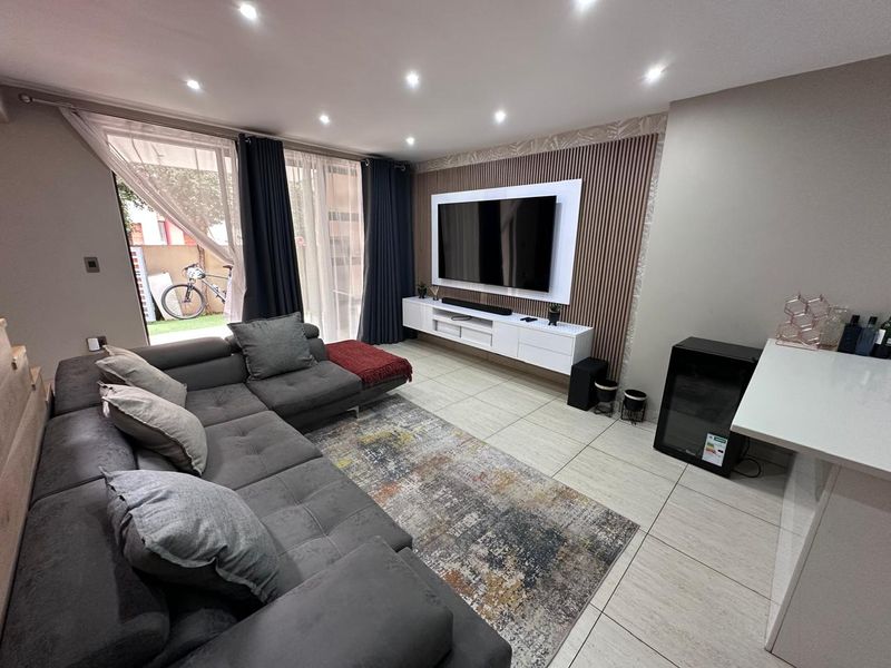 Modern living room featuring tiled floors, recessed lighting, and a stylish slatted timber feature wall with a built-in media console and sliding door access.