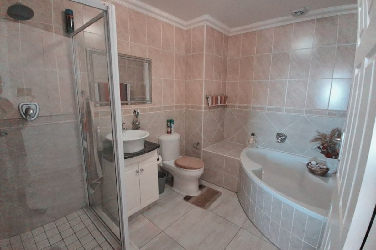 A functional bathroom featuring a separate shower enclosure, a built-in corner bathtub, a vanity with a vessel sink, and neutral wall and floor tiling.