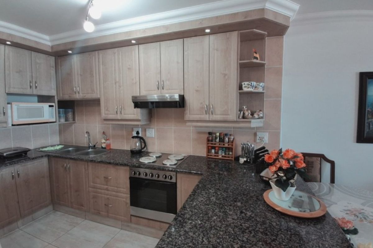 A functional kitchen featuring granite countertops, wooden cabinetry, built-in oven, hob, extractor fan, and a tiled backsplash with integrated microwave.