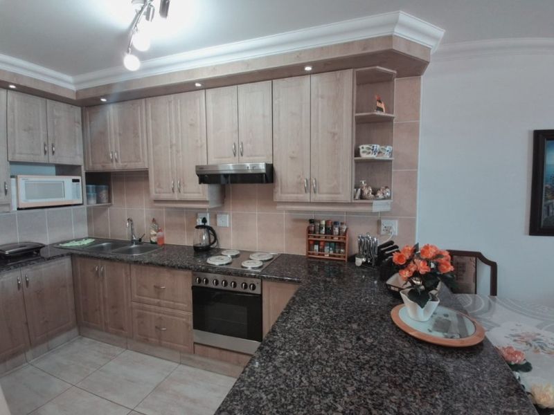 A functional kitchen featuring granite countertops, wooden cabinetry, built-in oven, hob, extractor fan, and a tiled backsplash with integrated microwave.