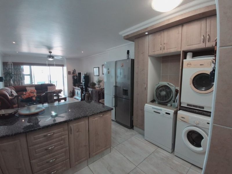 Open plan living area featuring a kitchen with granite island, built-in cabinetry, and tiled flooring, flowing into a spacious lounge with sliding door access.