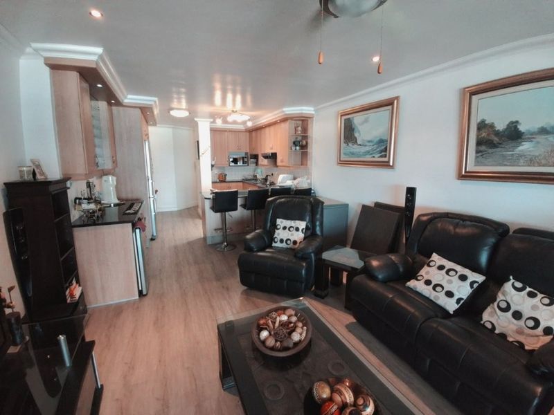 An open-plan living and kitchen area featuring light wood cabinetry, granite countertops, a breakfast bar, and laminate flooring throughout.