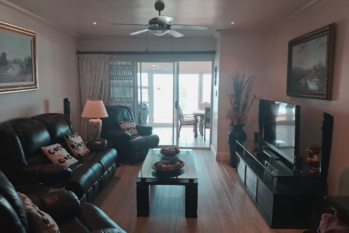 A comfortable living room featuring laminate flooring, recessed lighting, a ceiling fan, and sliding glass doors leading to an outdoor patio area.