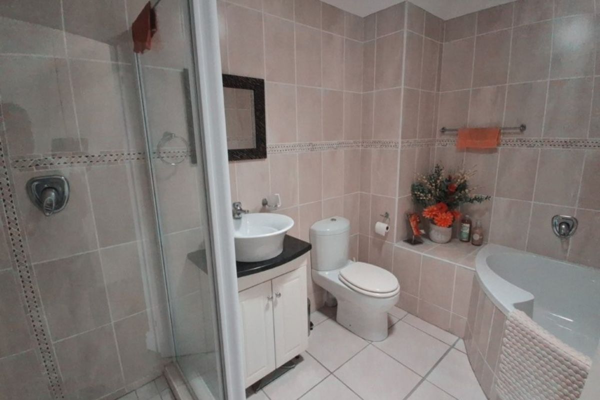 A functional bathroom featuring a shower enclosure, built-in bathtub, vanity with vessel sink, and neutral wall and floor tiling.