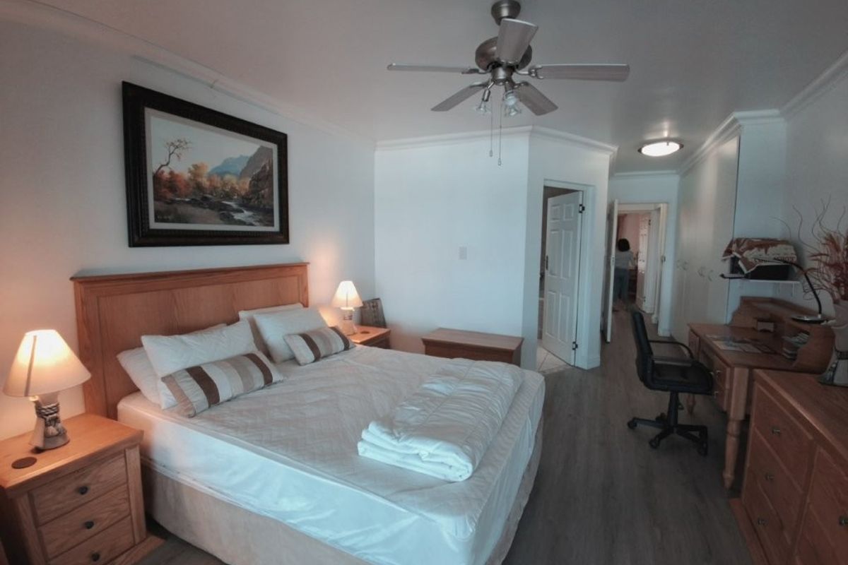 A well-maintained bedroom featuring laminate flooring, a ceiling fan, and built-in storage cupboards, offering a comfortable and functional living space.