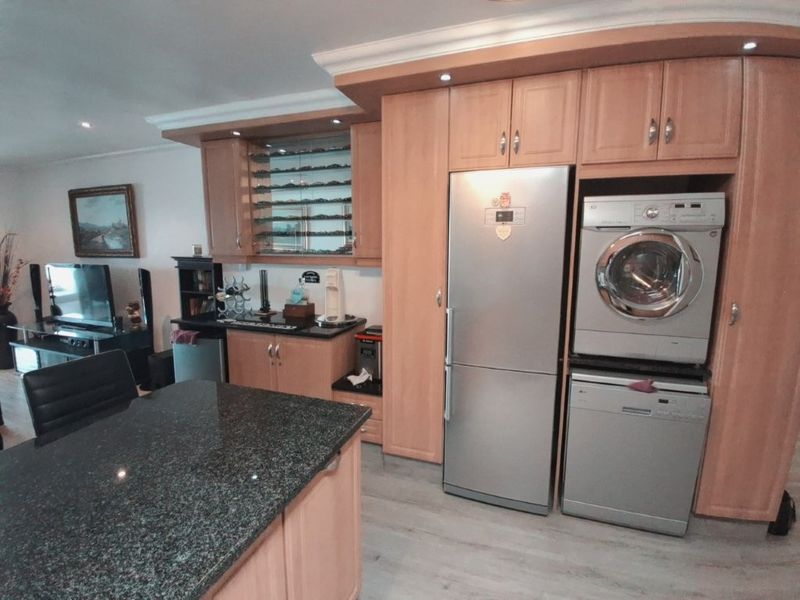 Open plan kitchen and living area featuring light wood cabinetry, granite countertops, integrated appliance housing, and modern laminate flooring.