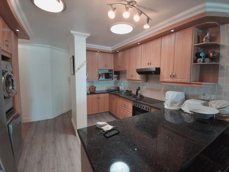 A functional kitchen featuring granite countertops, ample built-in cabinetry, integrated appliances, and a dedicated laundry area with a built-in washing machine.