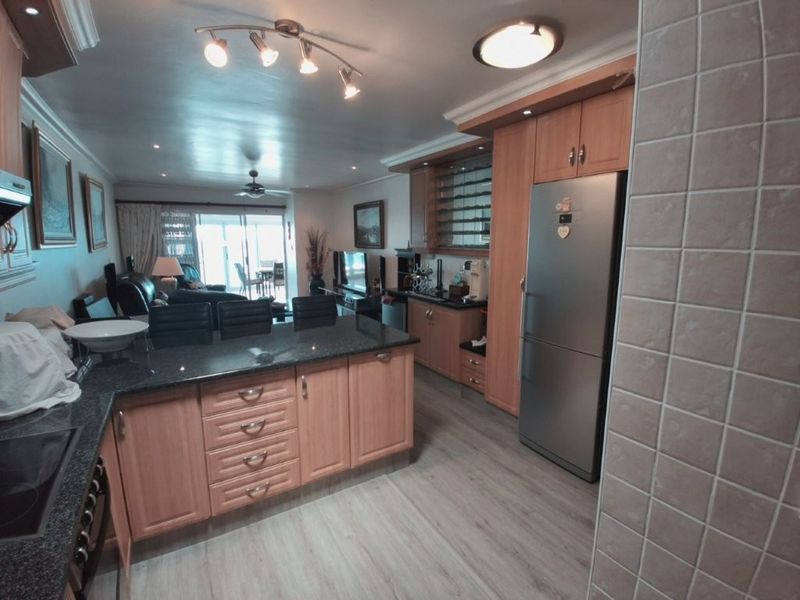 Open-plan kitchen and living area featuring wooden cabinetry, granite countertops, and laminate flooring, creating a functional and connected living space.