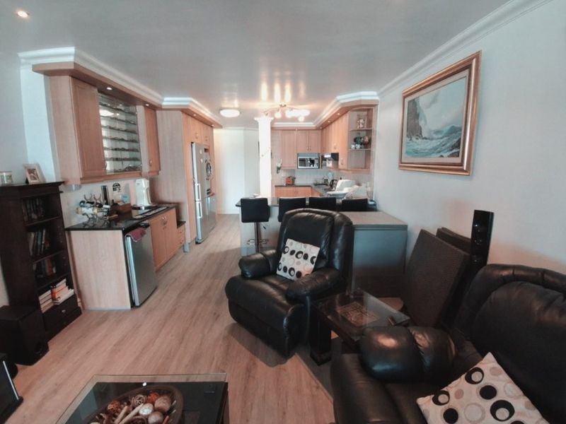 Open-plan living and kitchen area featuring light wood cabinetry, granite countertops, a breakfast bar, and laminate flooring with recessed lighting.