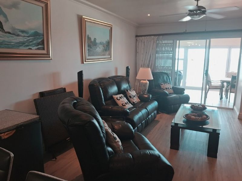 A comfortable living room featuring laminate flooring, a ceiling fan, and large sliding glass doors that provide access to an outdoor balcony area.