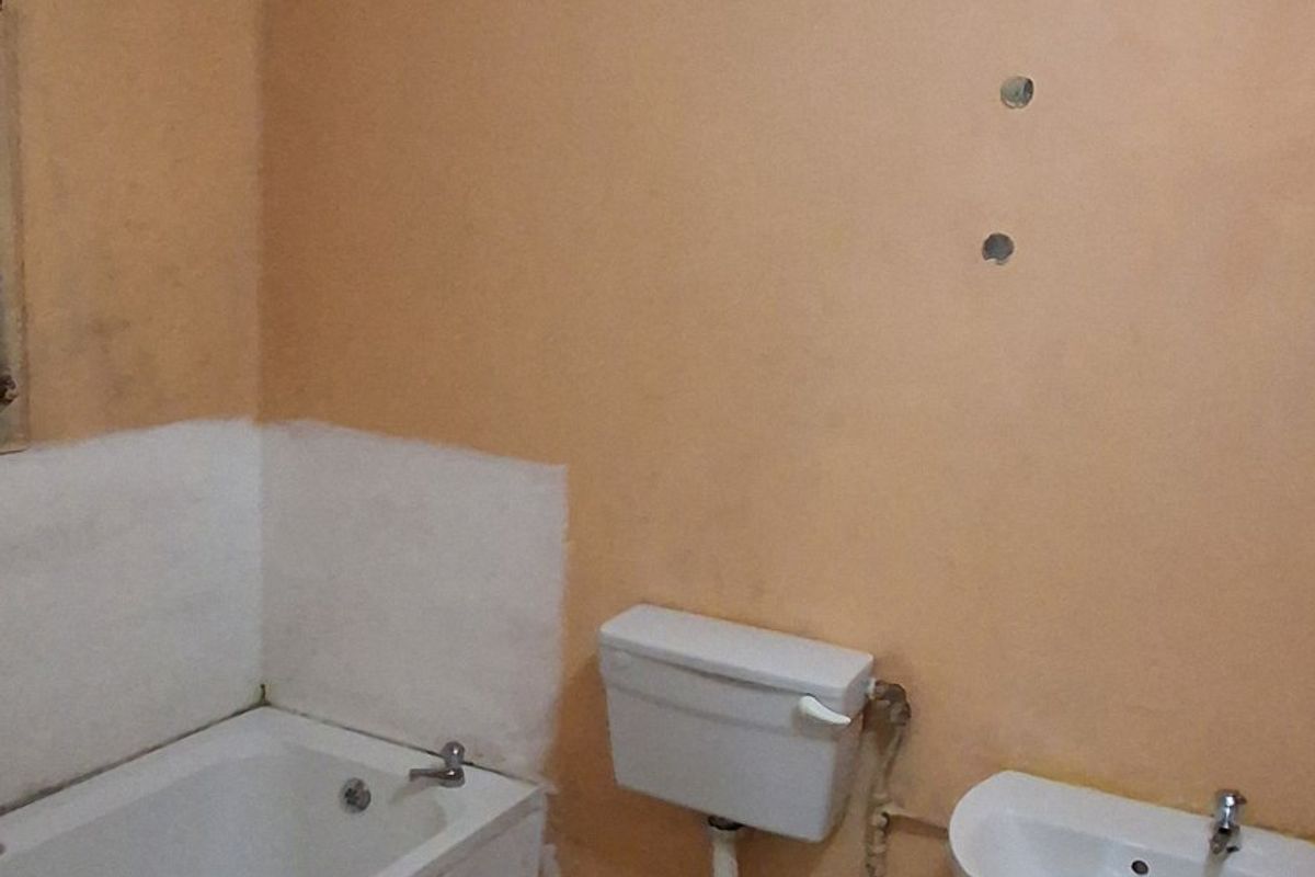 A dated bathroom featuring a standard bathtub, toilet, and pedestal sink, requiring cosmetic updates and wall refinishing to improve its overall condition.