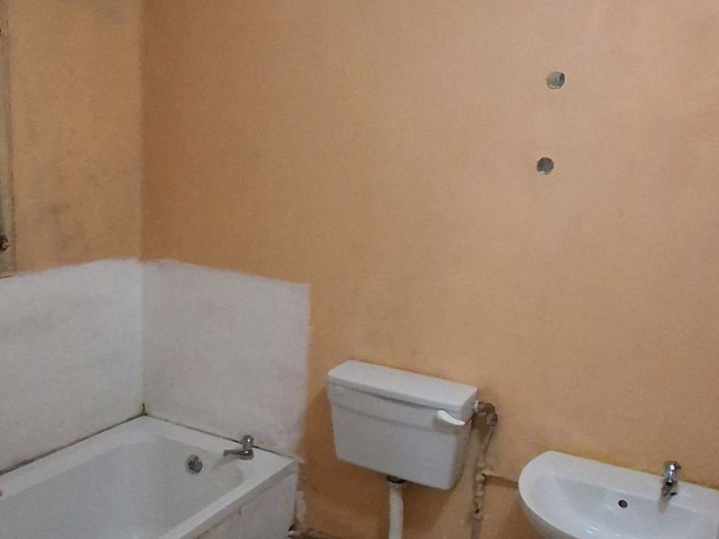 A dated bathroom featuring a standard bathtub, toilet, and pedestal sink, requiring cosmetic updates and wall refinishing to improve its overall condition.