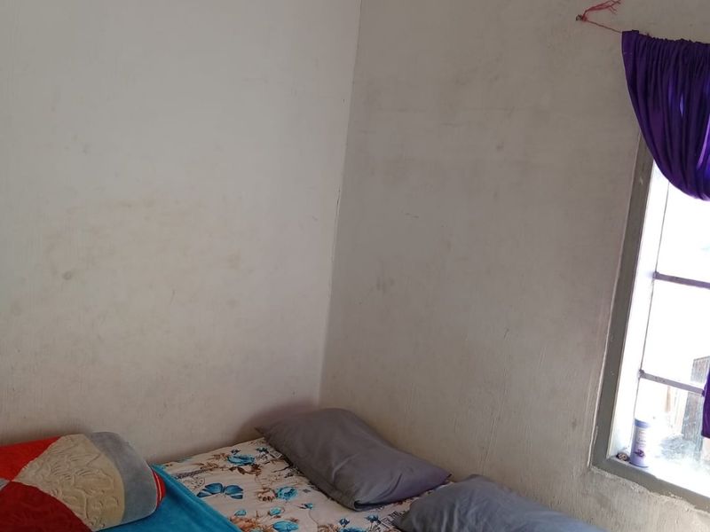 A compact bedroom featuring a window with natural light, requiring cosmetic updates to the wall finishes to improve the overall aesthetic.