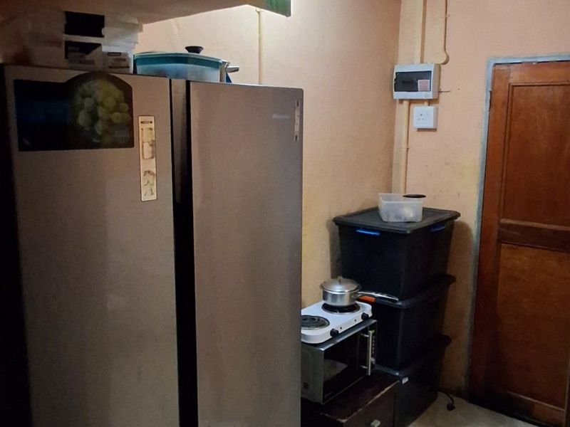 A small kitchen area featuring tiled flooring, a wooden door, and an exposed electrical distribution board, requiring cosmetic updates and improved lighting.