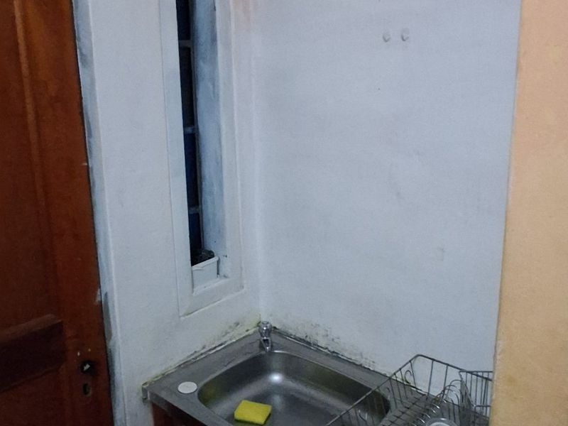 A small utility or scullery area featuring a stainless steel sink, tiled flooring, and unfinished wall surfaces requiring cosmetic attention.