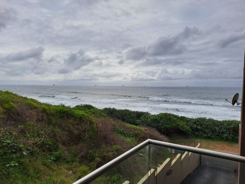 A scenic elevated view of the ocean and coastline, captured from a balcony with a modern glass and steel balustrade.