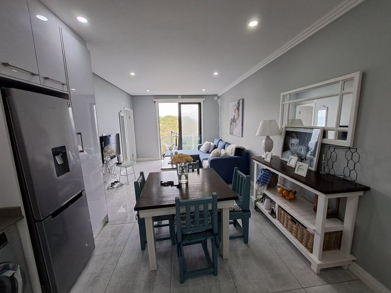 Modern open-plan living area featuring sleek tiled floors, recessed lighting, and seamless access to a balcony through sliding glass doors.