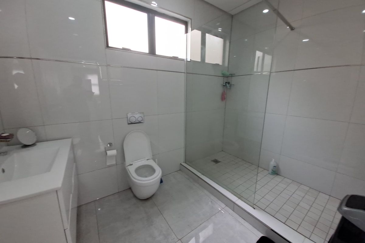 Modern bathroom featuring a wall-mounted toilet, a spacious walk-in shower with a glass enclosure, and a sleek vanity basin with tiled finishes.