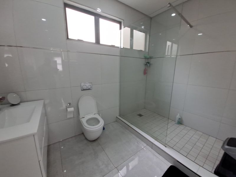 Modern bathroom featuring a wall-mounted toilet, a spacious walk-in shower with a glass enclosure, and a sleek vanity basin with tiled finishes.