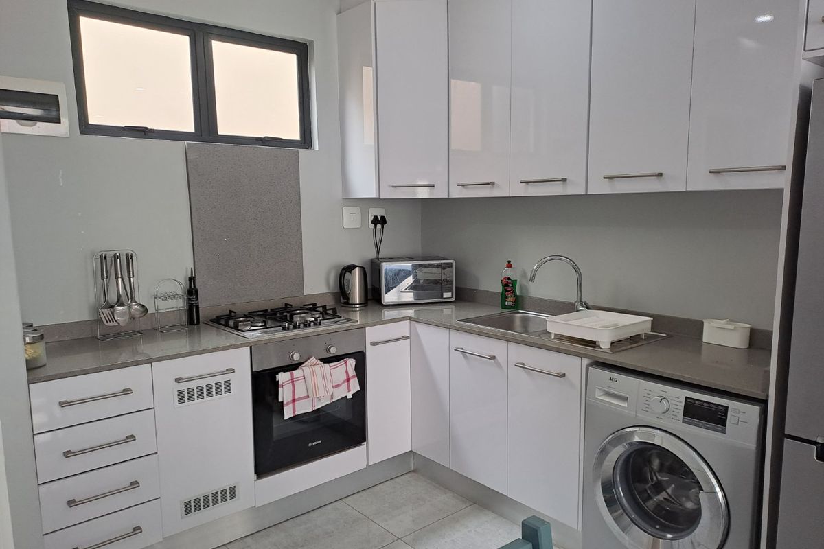 A modern, compact kitchen featuring white cabinetry, stone countertops, a gas hob, built-in oven, and integrated laundry appliance space.