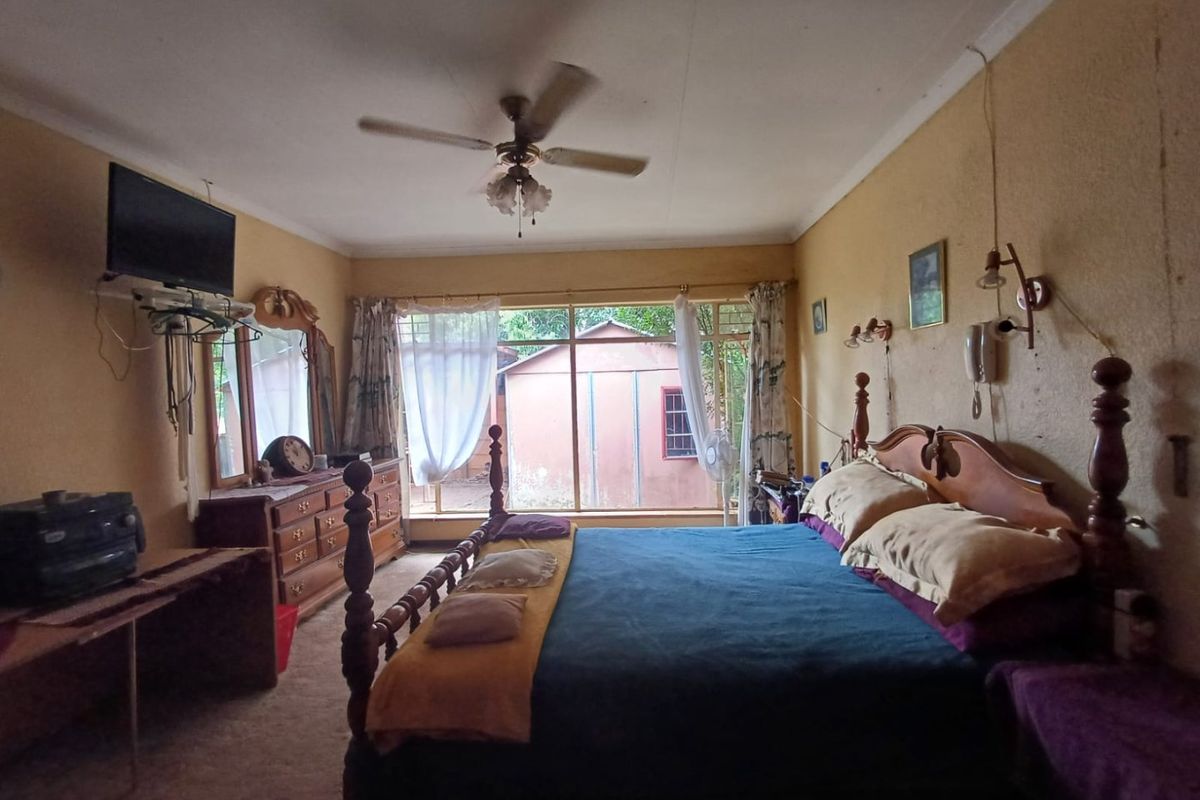 A spacious bedroom featuring a ceiling fan and large window, requiring cosmetic updates to the walls and ceiling to improve its overall condition.