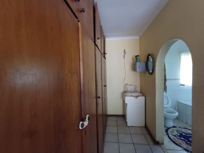A hallway featuring extensive built-in wooden cabinetry, tiled flooring, and an arched entryway leading into an adjoining bathroom.