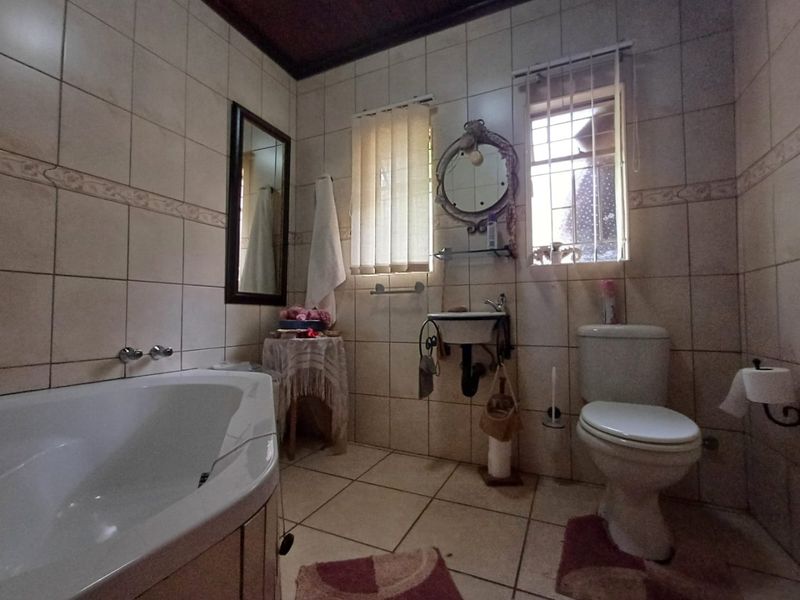 A functional bathroom featuring a corner bathtub, wall-mounted basin, and toilet, finished with neutral wall and floor tiling.