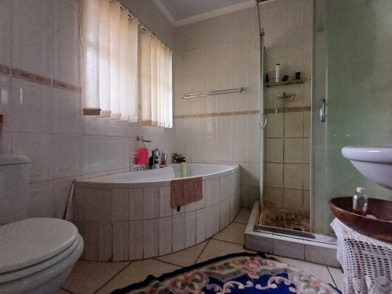 A functional bathroom featuring a built-in corner bathtub, a separate shower enclosure, and tiled finishes throughout.