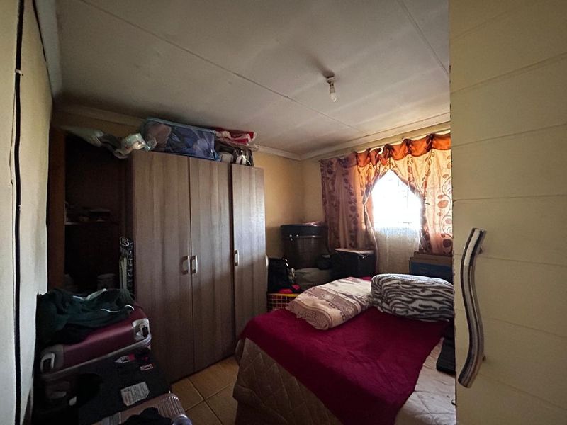 A compact bedroom featuring tiled flooring and a built-in wardrobe, offering a functional space with potential for cosmetic updates.