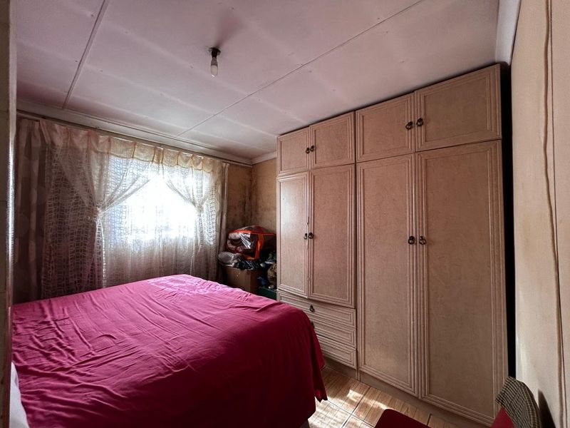A bedroom featuring built-in wardrobes and tiled flooring, currently showing significant wall damage and staining requiring maintenance and refurbishment.