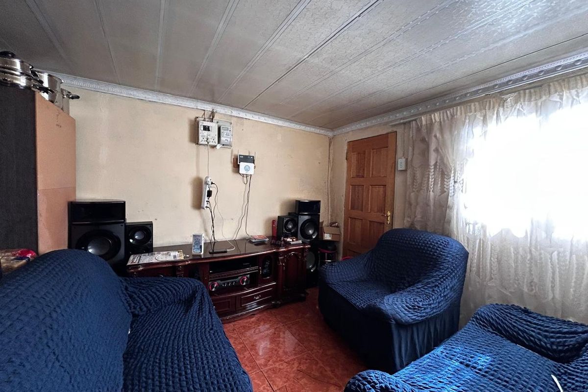 A living room featuring tiled flooring, a timber door, and textured ceiling finishes, currently requiring cosmetic updates to the walls and electrical fixtures.