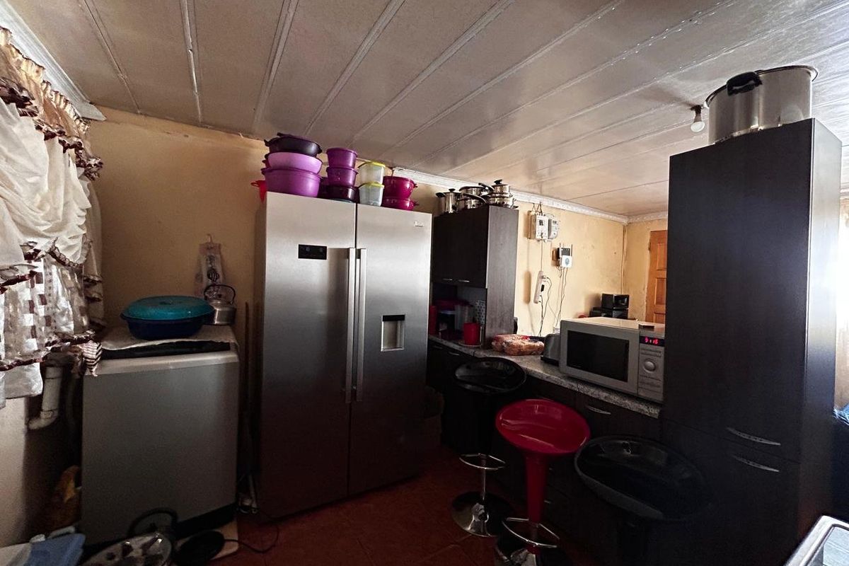 A compact kitchen area featuring built-in cabinetry, tiled flooring, and a panelled ceiling, currently showing signs of wear and dated finishes.