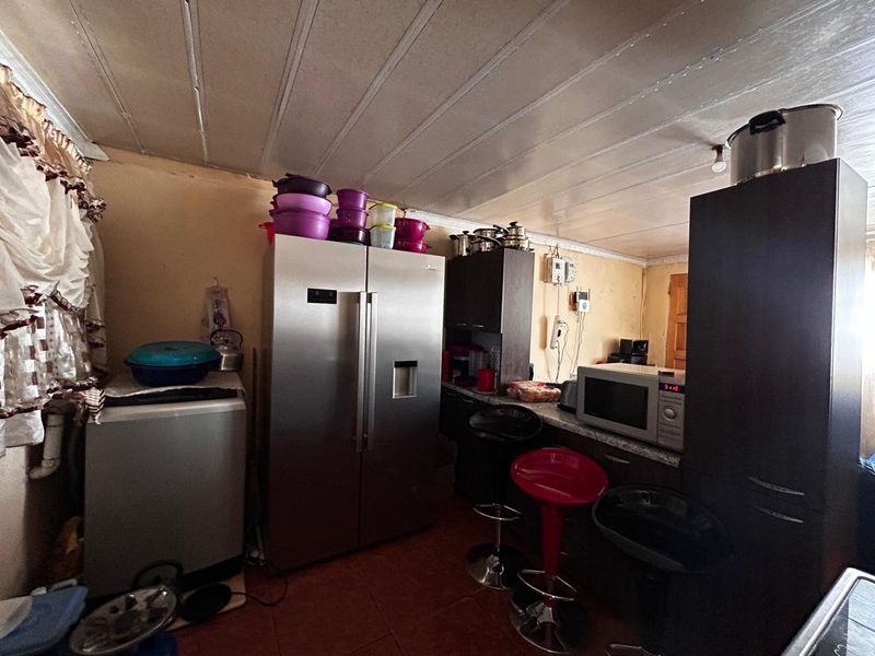 A compact kitchen area featuring built-in cabinetry, tiled flooring, and a panelled ceiling, currently showing signs of wear and dated finishes.