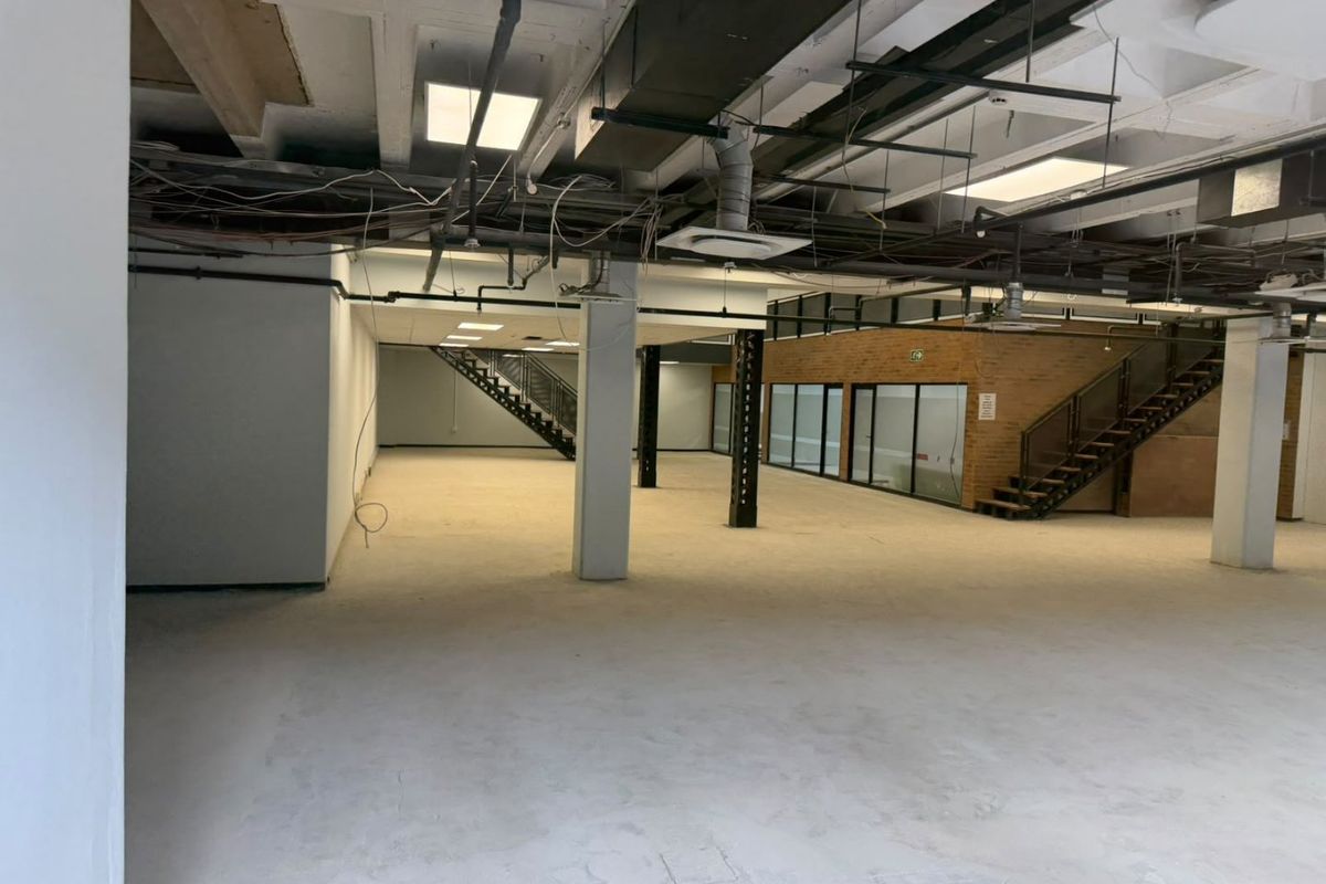 Expansive open-plan commercial space featuring exposed industrial ceilings, structural columns, and internal staircases, offering a versatile layout for office or retail use.