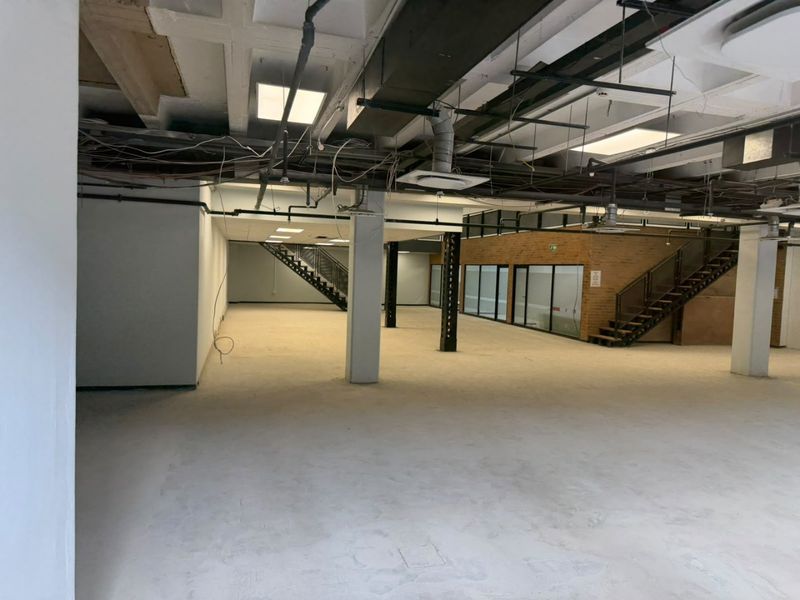 Expansive open-plan commercial space featuring exposed industrial ceilings, structural columns, and internal staircases, offering a versatile layout for office or retail use.