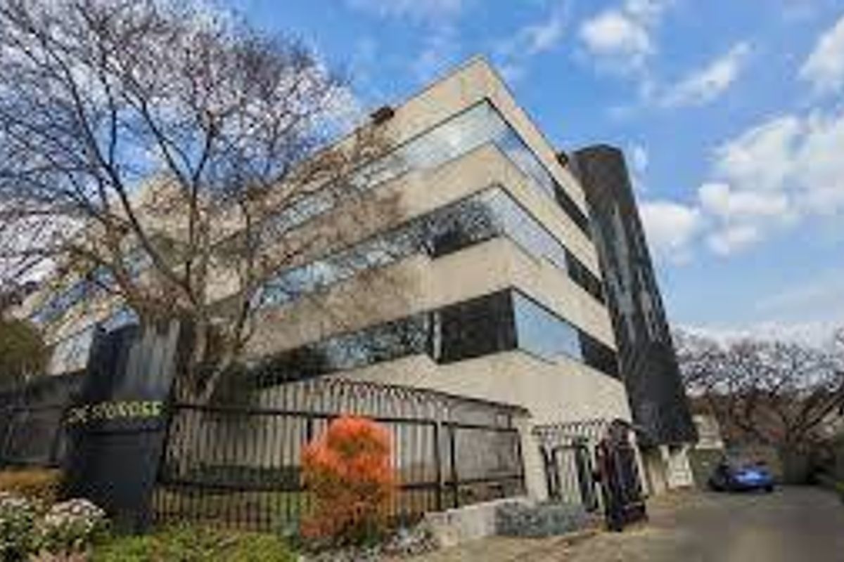 A multi-story commercial office building featuring a modern glass facade, secure gated entrance, and paved driveway access.