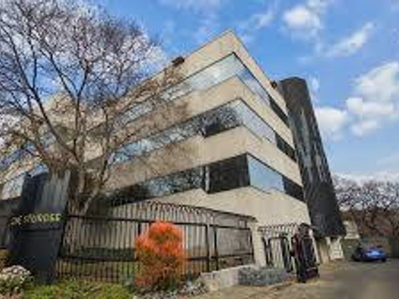 A multi-story commercial office building featuring a modern glass facade, secure gated entrance, and paved driveway access.
