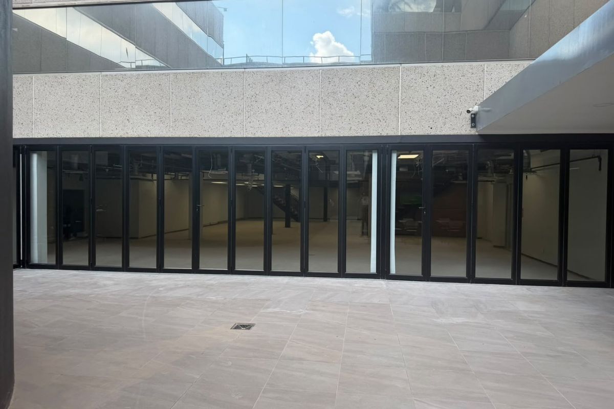 A modern commercial exterior space featuring a tiled patio area with large bi-fold glass doors providing access to the interior office or retail space.