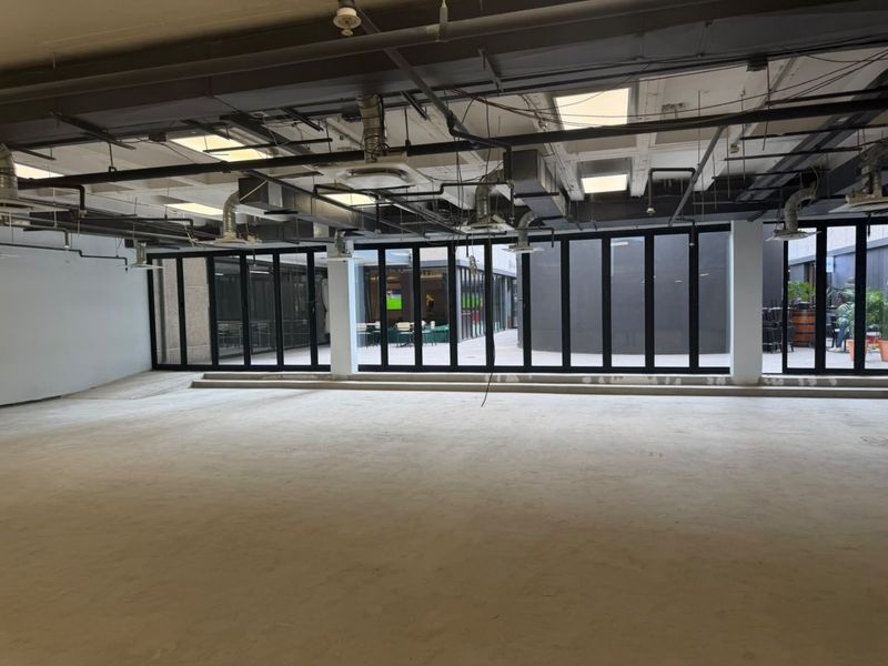Spacious open-plan commercial area featuring exposed industrial ceilings, HVAC ducting, and large bi-fold glass doors opening to an outdoor courtyard.