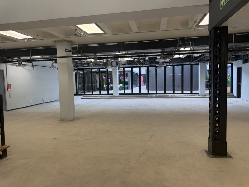 Spacious open-plan commercial area featuring exposed industrial ceilings, concrete flooring, and large glass sliding doors providing access to an outdoor courtyard.